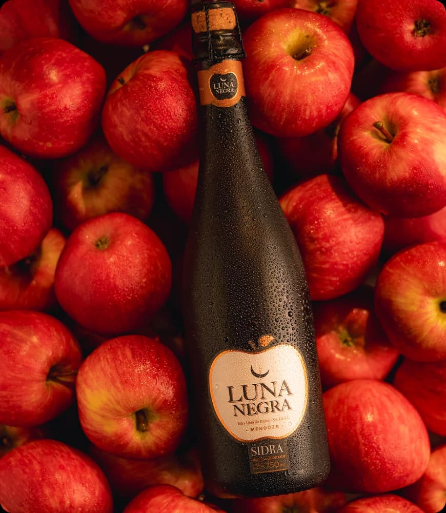Botella de sidra Luna Negra rodeada de manzanas rojas